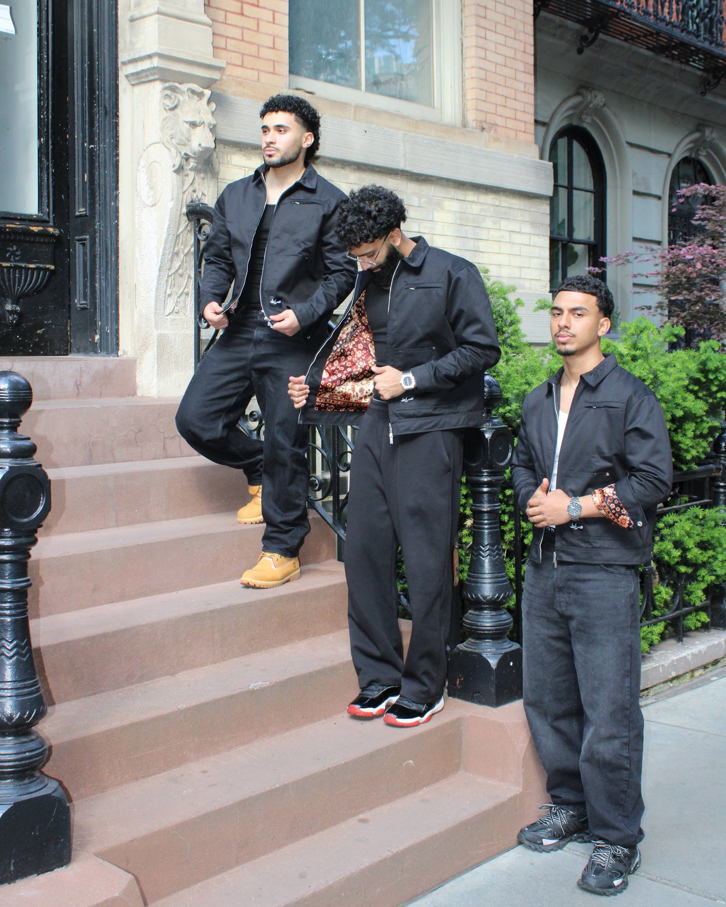 Three men in black outfits standing on a set of stairs in an urban setting.
