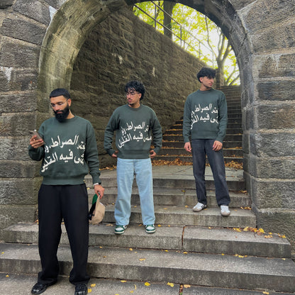 Three individuals wearing matching green sweatshirts standing on stone steps with a stone archway in the background.